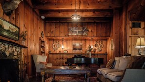 A cozy room with wooden walls, a piano, a sofa, and a coffee table. - Sierra Sky Ranch (Oakhurst)