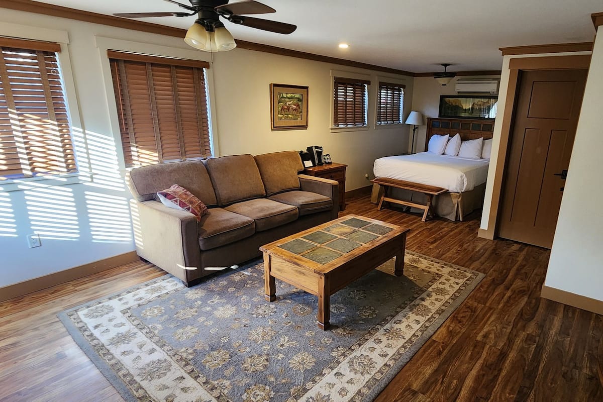 A well-lit living room with a sofa, a coffee table, a bed, and a television.