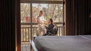 A room with a bed, a wooden deck, and a sliding glass door leading to an outdoor area with trees. - Sierra Sky Ranch (Oakhurst)