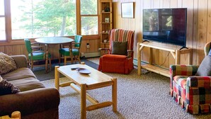 Una sala de estar acogedora con detalles de madera, un televisor grande y un comedor con sillas verdes.