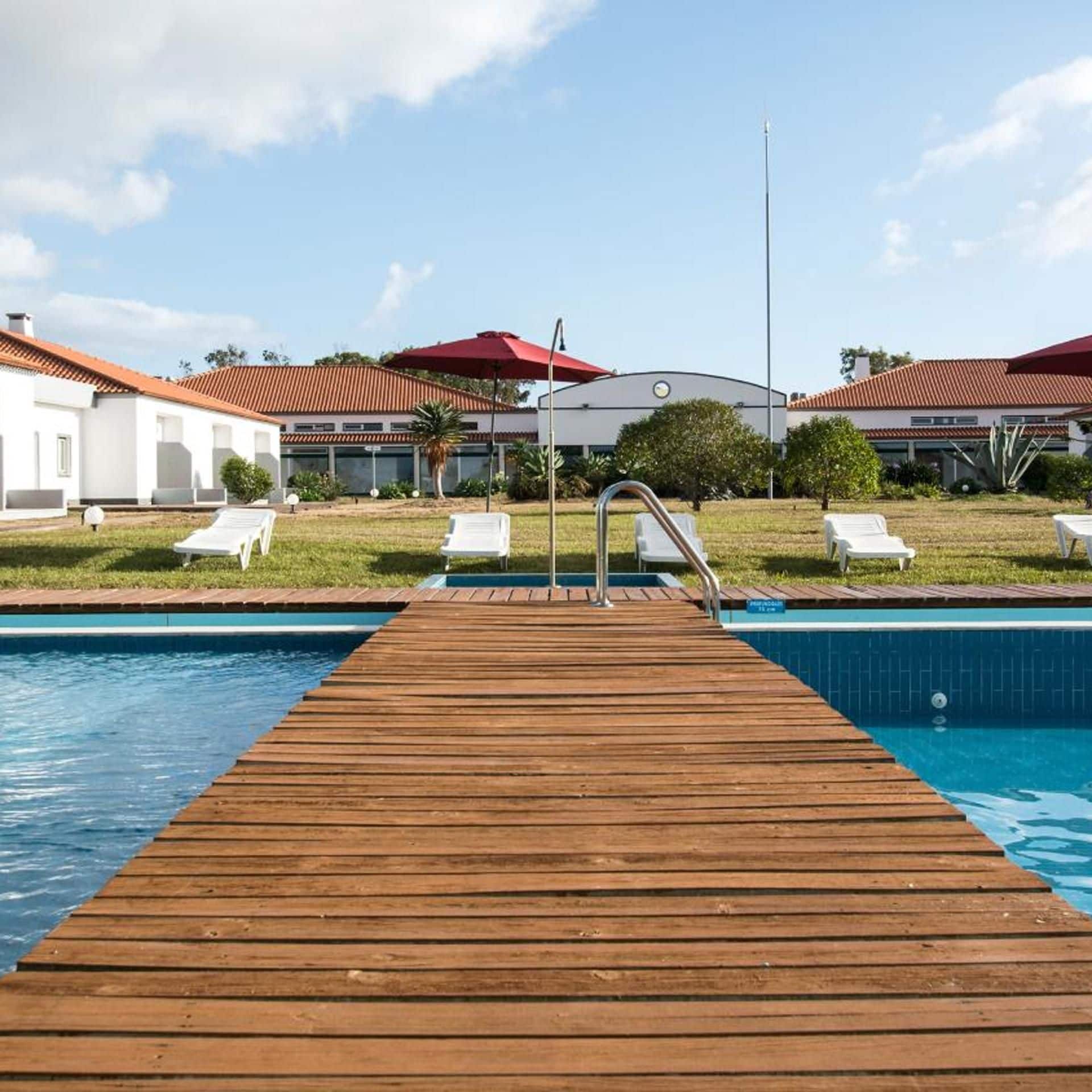 A wooden deck leading to a swimming pool with lounge chairs and umbrellas.