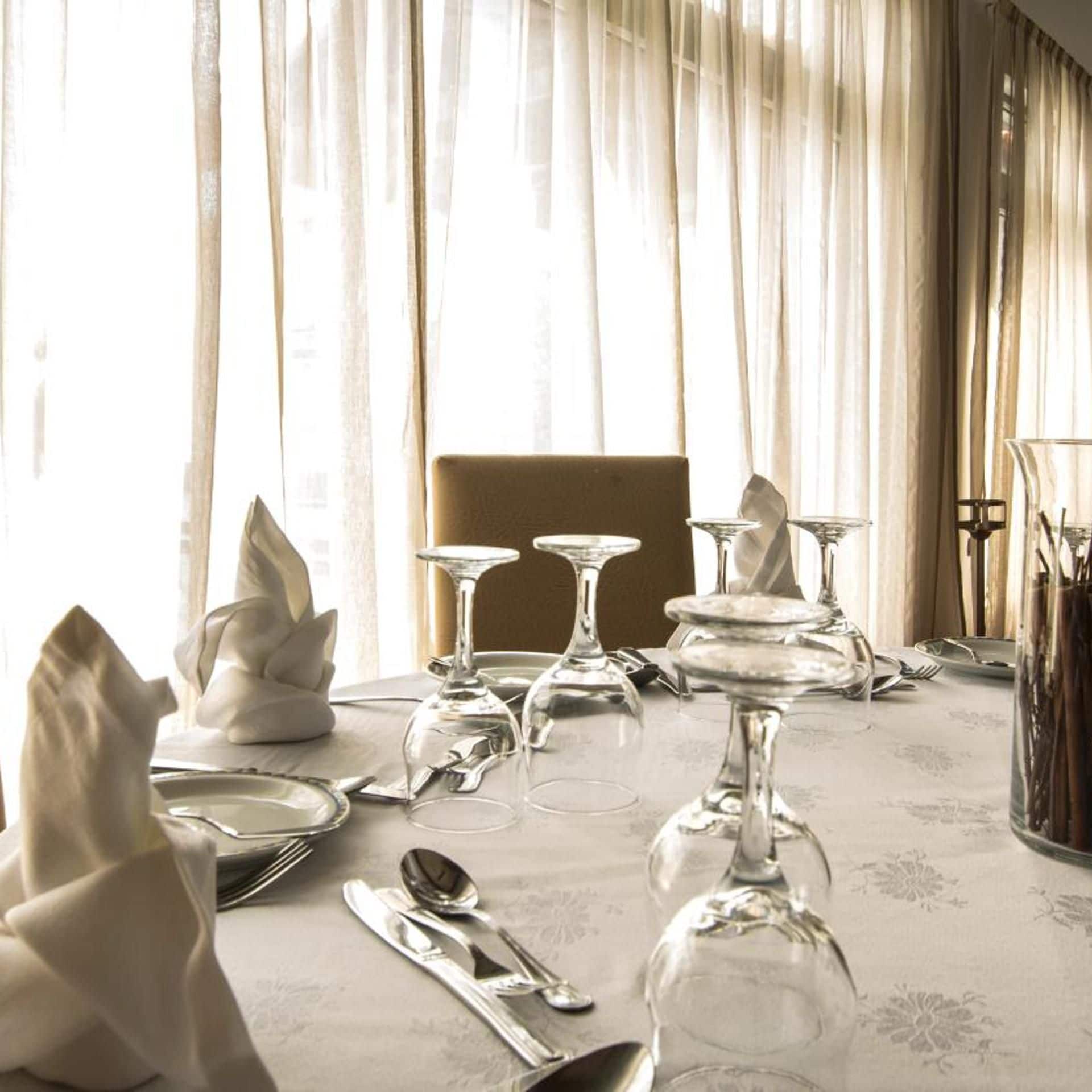 A dining table set with silverware, wine glasses, and a vase with a white flower arrangement.