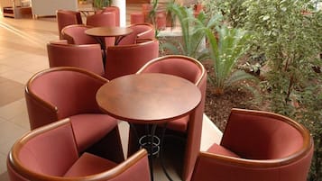 A seating area with round tables and cushioned chairs, surrounded by greenery.