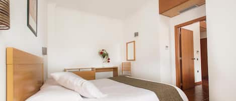 Un dormitorio con cama, escritorio y silla. Hay una puerta que da a otra habitación.