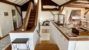 Una stanza in stile loft con una scala in legno, un tavolino e una collezione di cimeli marittimi, tra cui un modellino di nave e una bandiera americana.