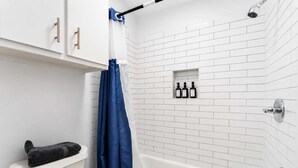 Een badkamer met witte betegelde wanden, een badkuip, een toilet en een douchegordijn.