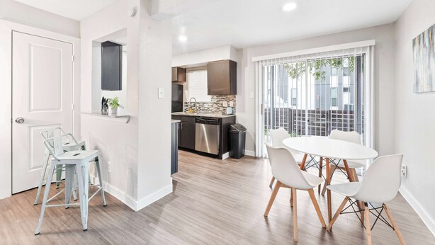 Una cucina moderna con elettrodomestici in acciaio inossidabile, un'area pranzo con sedie bianche e vista sulla città attraverso ampie finestre.