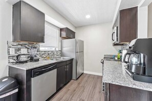 Compact kitchen with a modern design, featuring a refrigerator, dishwasher, microwave, and sink.