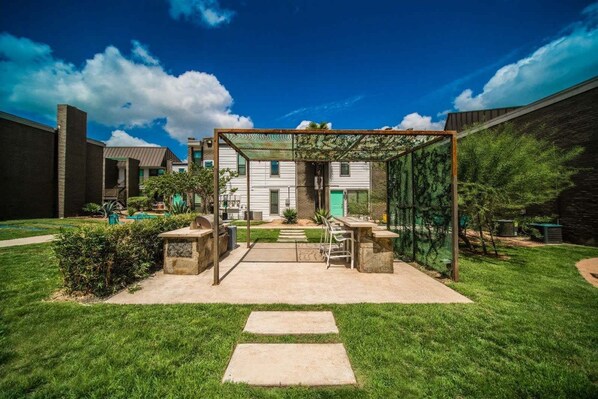 Relax in a serene outdoor space surrounded by lush greenery and a pergola, perfect for unwinding with a table and chairs.