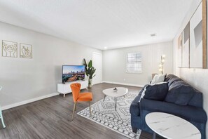Relax in this stylish living room with a sofa, coffee table, and TV stand, surrounded by a large window and a potted plant.