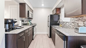 Una cucina moderna con pensili in legno scuro, un frigorifero in acciaio inossidabile, un forno a microonde, una macchina per il caffè e un tostapane.