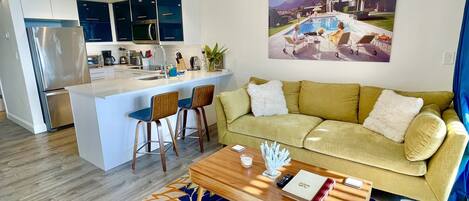 A modern living room with a sofa, coffee table, and a view of a kitchen and dining area.