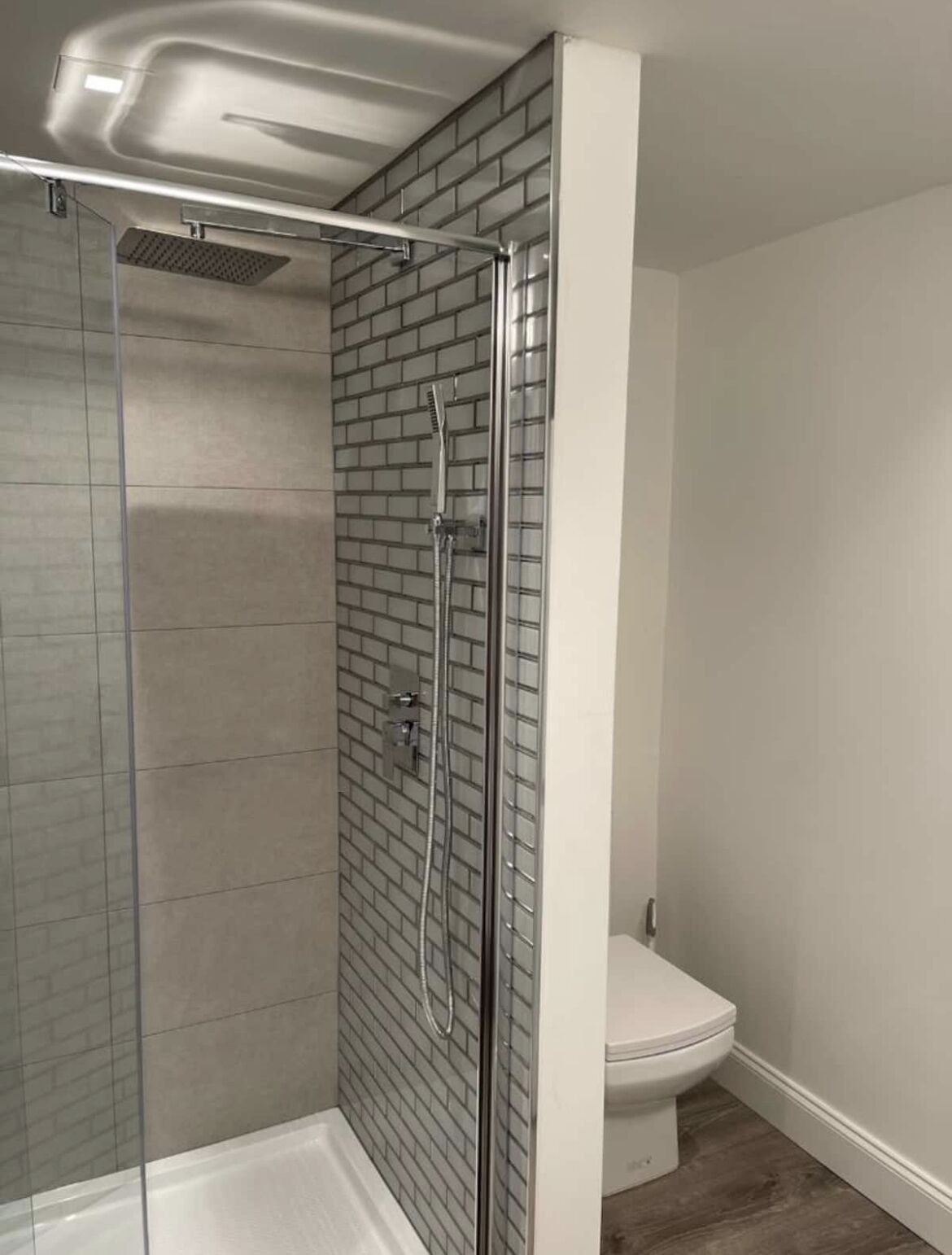 A shower with a glass door, a white toilet, and a tiled wall.