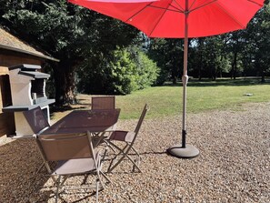 Ein Außenbereich mit Tisch und Stühlen, einem roten Sonnenschirm und einem Grill.