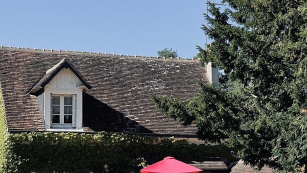 Ein Haus mit geneigtem Dach und Schornstein, sowie einem roten Regenschirm.