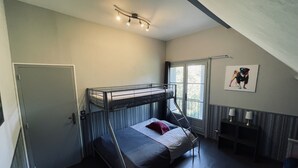 Ein Schlafsaalzimmer mit Etagenbetten, einem Schreibtisch, einem Stuhl, einem Fenster und einer Deckenleuchte.