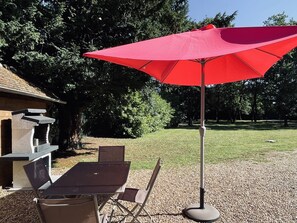 Ein Sitzbereich im Freien mit einem roten Sonnenschirm, einem Grill und einem Tisch mit Stühlen.