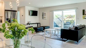 En moderne stue med en sort sofa, et glasbord og et spiseområde med et klart glasbord samt en vase med blomster.