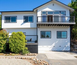 A two-story modern house with a balcony, large windows, and a well-maintained garden.