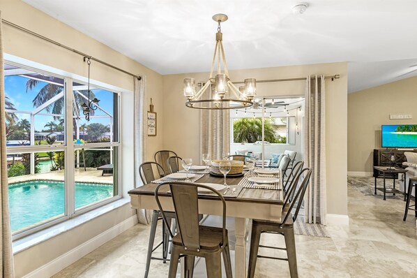 Enjoy meals with family and friends in this spacious dining area, surrounded by comfortable chairs and a stunning view of the outdoor pool and lush greenery.
