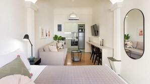 Ein modernes Hotelzimmer mit einem großen Bett, einer Sitzecke mit Sofa und Sesseln, einer kleinen Küchenzeile und einem Esstisch.