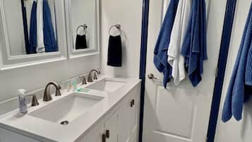 Un baño con dos lavamanos, un espejo y una puerta con toallas colgadas en ganchos.