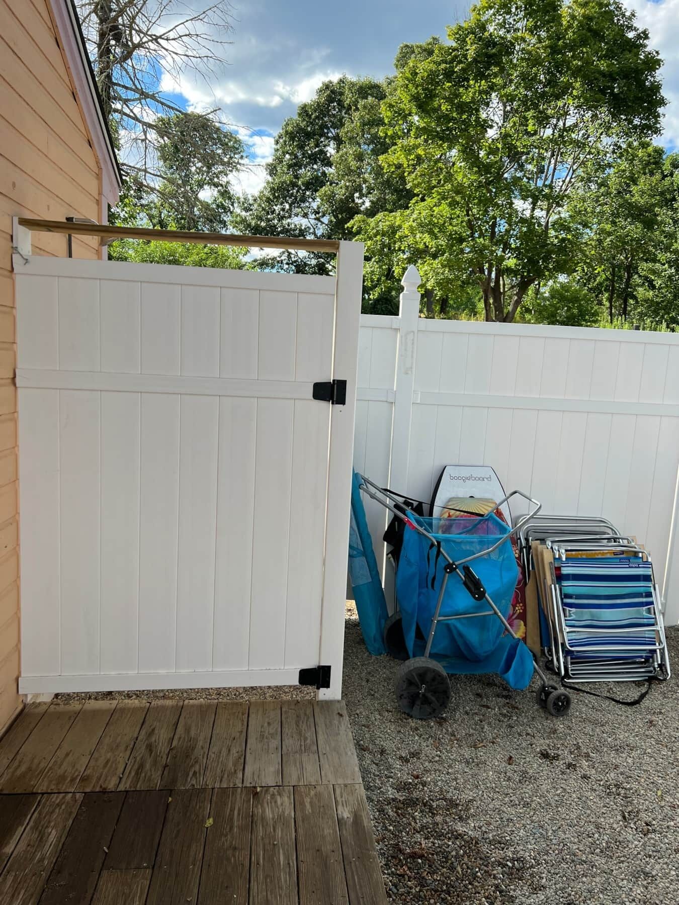 A wooden deck with a white fence, a blue bag, and a luggage cart.