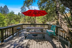 A wooden deck with a picnic table and a red umbrella, surrounded by trees. - Riverfront Paradise w/ Pool, Spa & Tennis Court (Oakhurst)