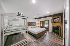 A bedroom with a bunk bed, a large bed, a fireplace, and a TV mounted on the wall. - Riverfront Paradise w/ Pool, Spa & Tennis Court (Oakhurst)