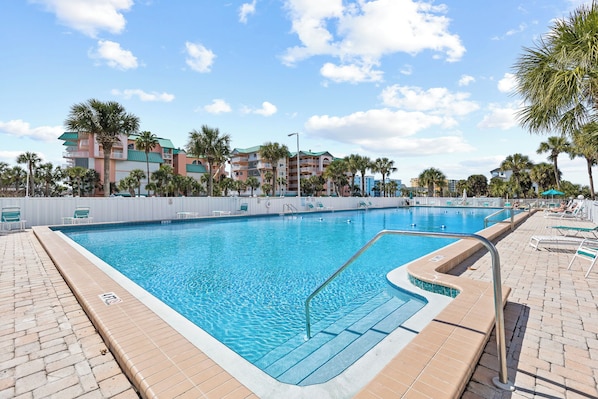 A swimming pool with clear blue water, surrounded by palm trees and a brick walkway.