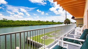 A balcony with white railings overlooking a river, surrounded by greenery and a clear sky. - Belleview Gulf Studio/Steps away from BEACH (378) (Indian Shores)