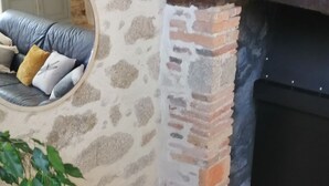 A corner of a room with a stone wall, a brick fireplace, and a yellow armchair with a geometric pillow.