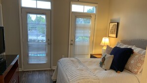 A bedroom with a bed, a nightstand, a lamp, a television, and two doors with blinds. - Fabulous One Bed/One Bath Corporate Furnished Apt in Alpharetta (Alpharetta)