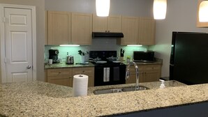 A modern kitchen with granite countertops, a stainless steel sink, a black refrigerator, and wooden cabinets. - Fabulous One Bed/One Bath Corporate Furnished Apt in Alpharetta (Alpharetta)