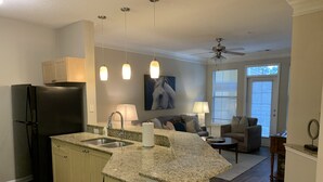 A modern kitchen with granite countertops, a black refrigerator, and a dining area with a gray sofa and a small table. - Fabulous One Bed/One Bath Corporate Furnished Apt in Alpharetta (Alpharetta)