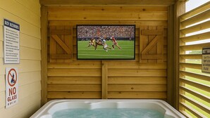 Un bain à remous dans un chalet en bois, avec un téléviseur fixé au mur diffusant un événement sportif.