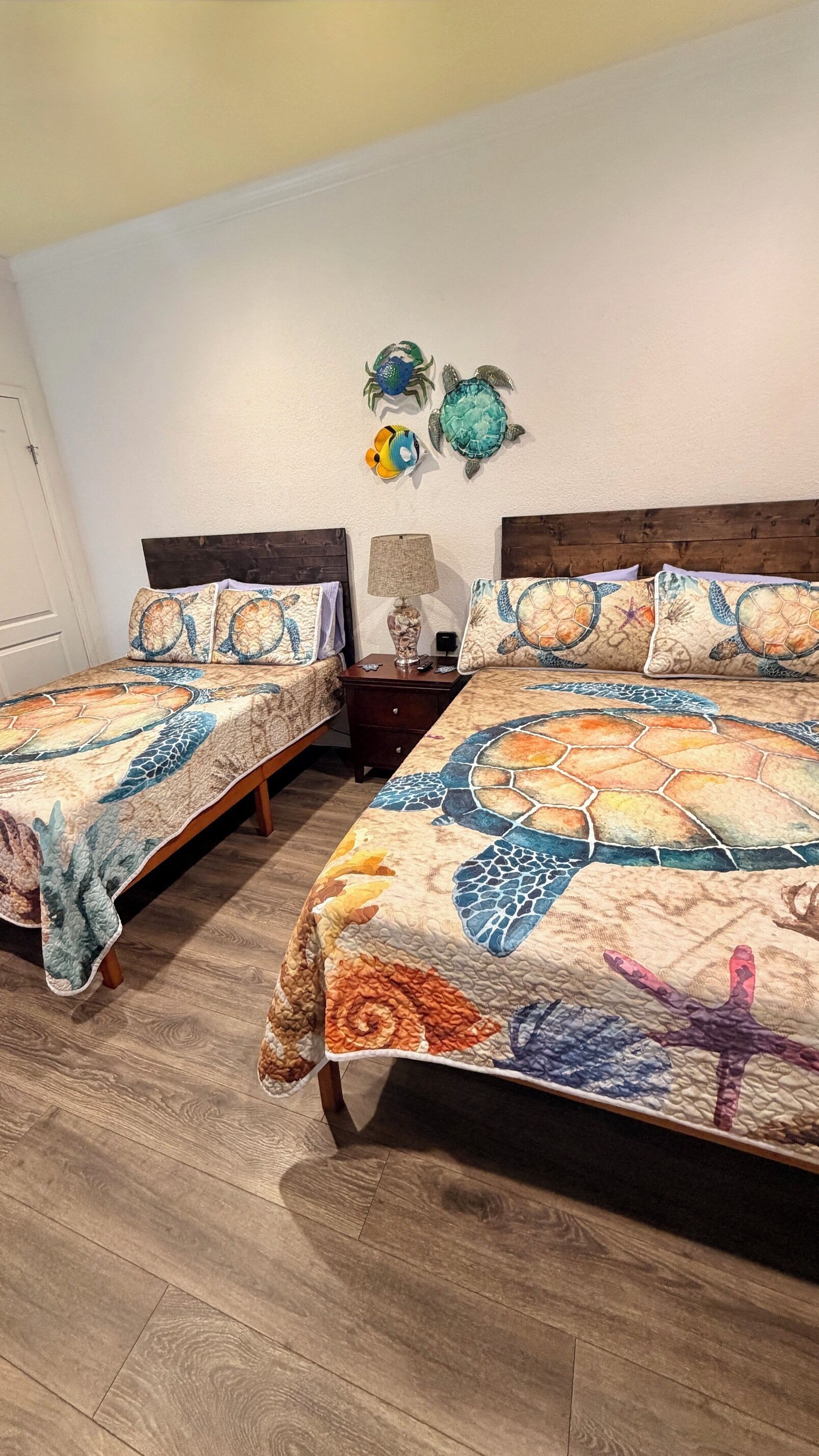 Une chambre à coucher avec deux lits, chacun recouvert d’une couvre-lit à motifs, une table de chevet avec une lampe et des œuvres d’art décoratives accrochées au mur.