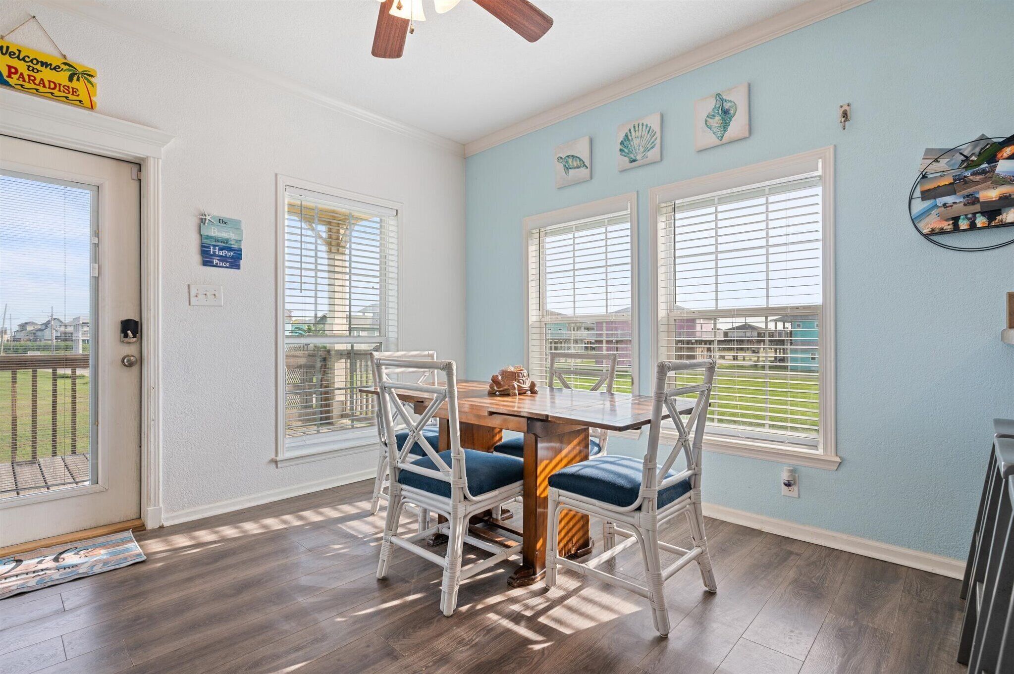 A dining area with a table and chairs, large windows with blinds, and a view of a green landscape.