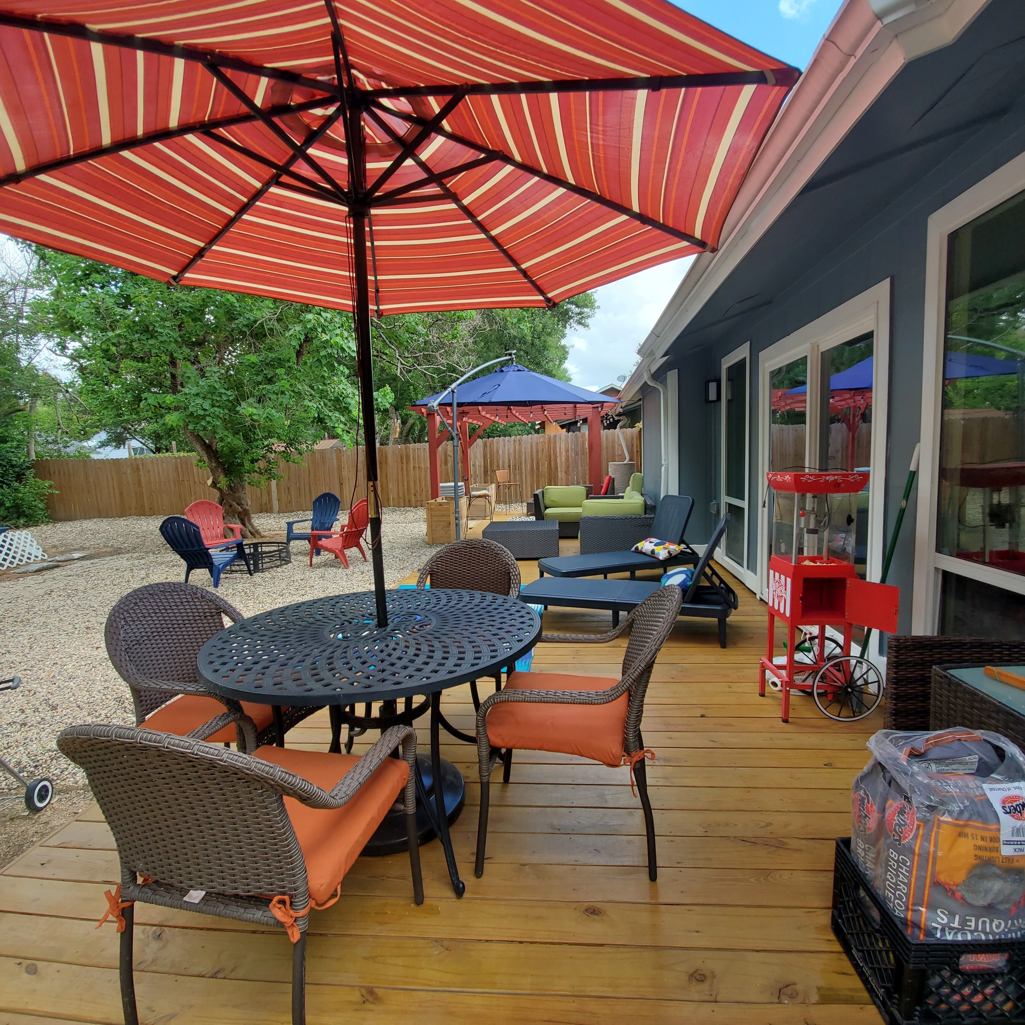 Une terrasse extérieure avec une table ronde et des chaises, un parasol à rayures rouges et blanches, et une plateforme en bois.