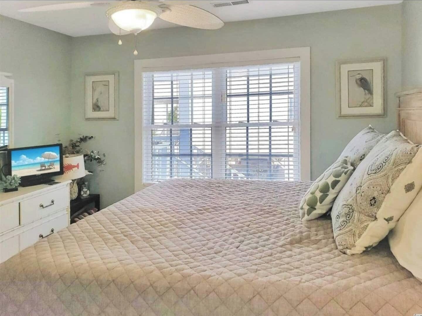 Un dormitorio con una cama grande, un televisor sobre un tocador y una ventana con persianas.