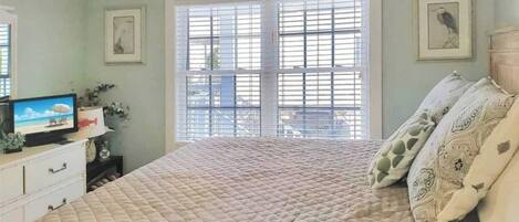 Un dormitorio con una cama grande, un televisor sobre un tocador y una ventana con persianas.