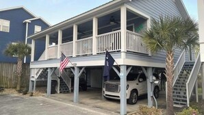 A two-story house with a covered porch, a flag, and a parked SUV. - Beach house with pool only steps from the ocean (Murrells Inlet)