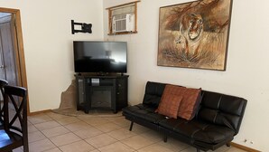 Een woonkamer met een zwarte leren bank, een flatscreen televisie op een standaard, een schilderij van een tijger en een raam met zonwering.
