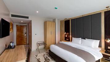 Una habitación de hotel moderna con una cama grande, un escritorio de madera, un televisor de pantalla plana y un armario.