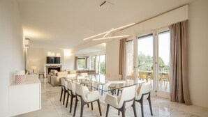 Ein moderner Essbereich mit einem Glastisch und Stühlen, eine Küche im Hintergrund und ein Balkon mit Vorhängen.
