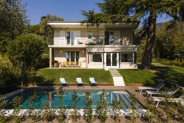 Une maison à deux étages avec une piscine, du mobilier d’extérieur et une pelouse bien entretenue.