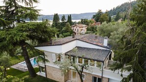 Ein modernes Haus mit Swimmingpool, umgeben von üppiger Vegetation und Blick auf den See.