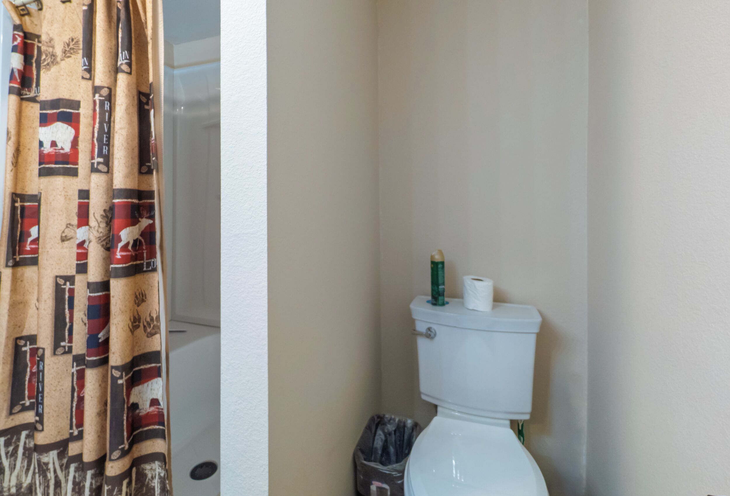 A bathroom with a toilet, a trash bin, and a shower curtain.