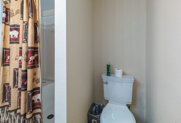 A bathroom with a toilet, a trash bin, and a shower curtain.