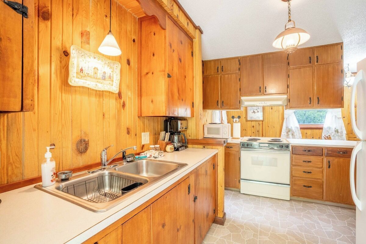 A kitchen with wooden cabinets, a stainless steel sink, a stove, and a microwave.